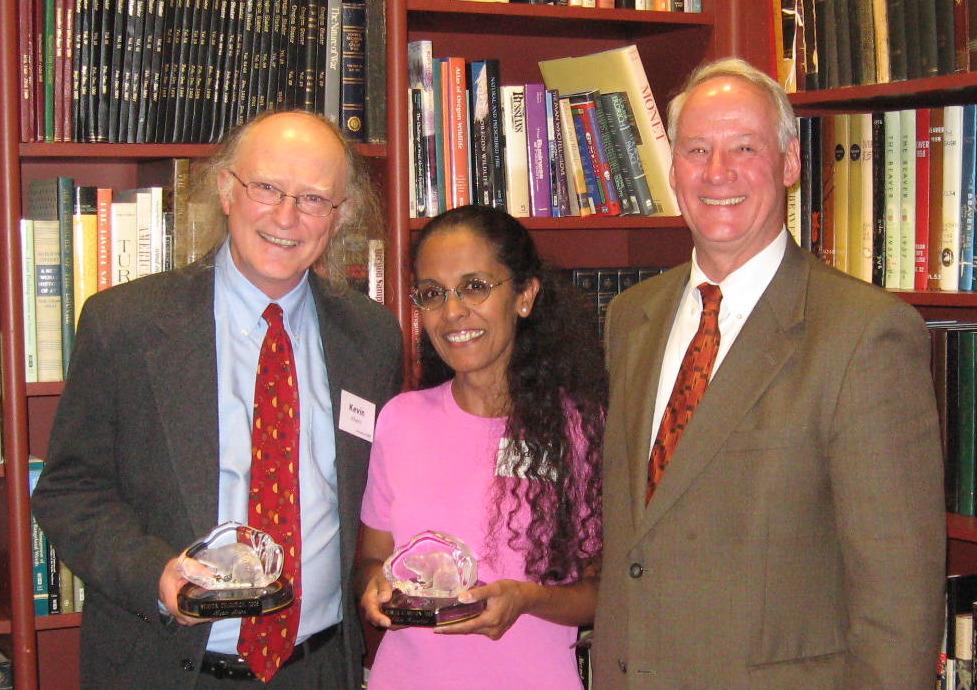 Kevin and Indira holding their Beaver Champion Awards next to Ed Ray in front of a bookshelf.