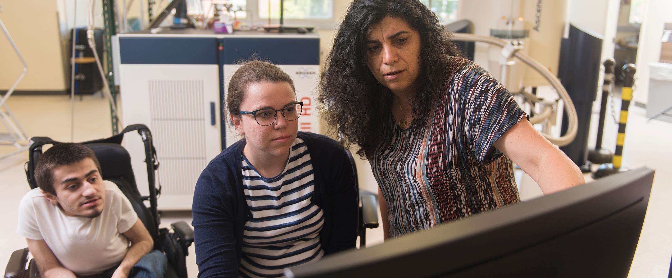Elisar Barbar analyzing lab data on a computer with two graduate students in her lab.