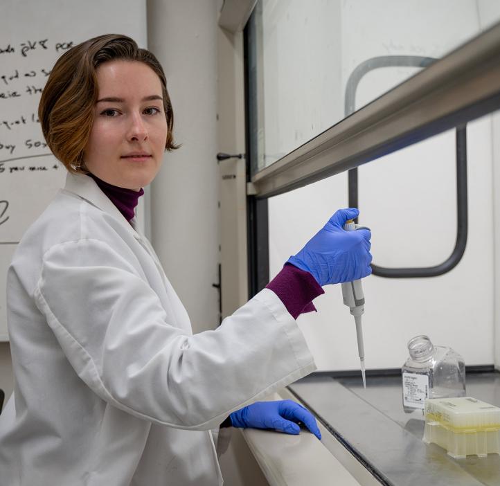 Elizaveta Zhivaya in a lab wearing a lab coat holding a pipette. 